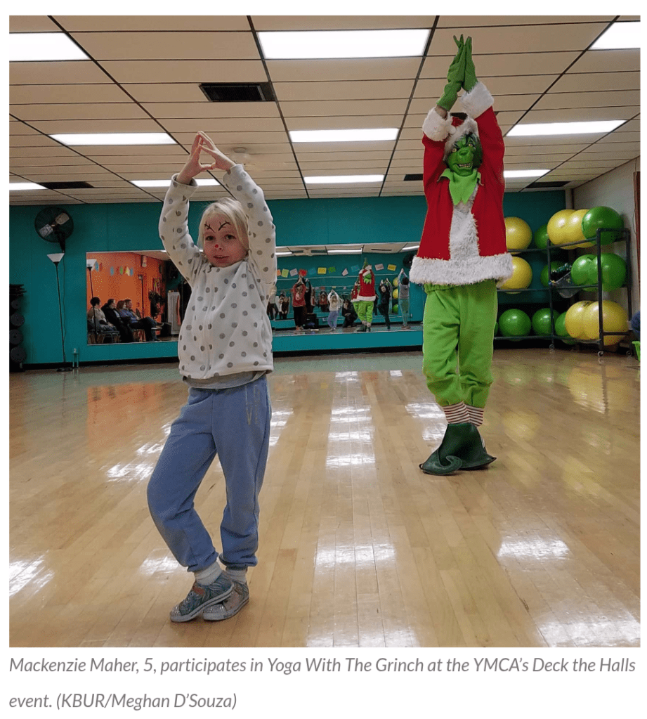 Little girl stands next to the Grinch as they do a standing yoga pose.